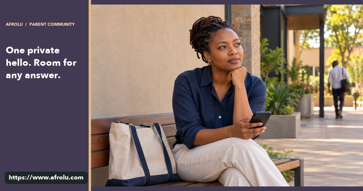 An adult parent pauses over a phone on a neighborhood bench near a community center.