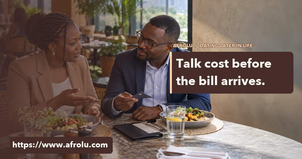 Two midlife adults discuss a lunch bill across a table; one holds a bank card.